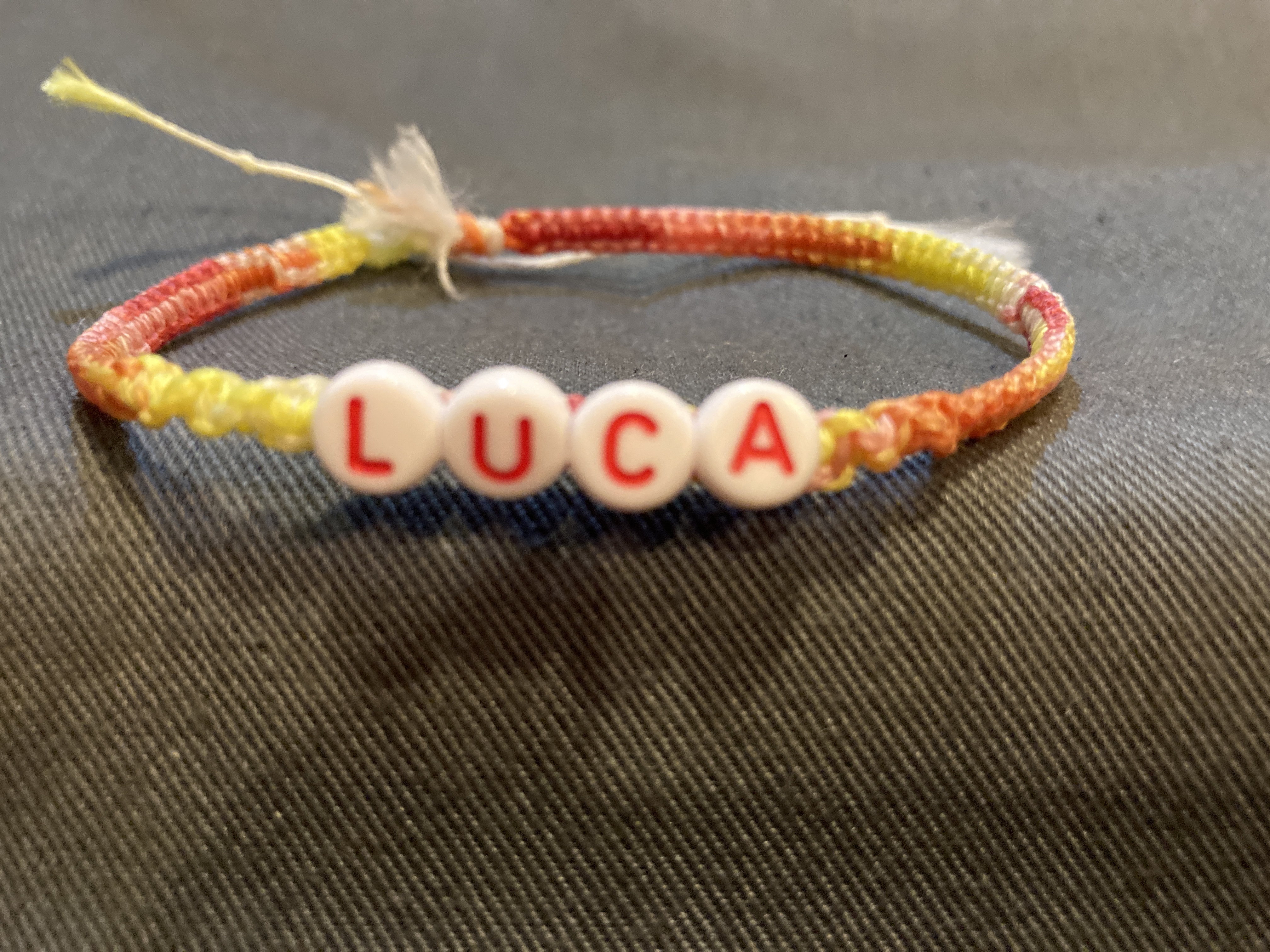 赤系グラデーション・白色の糸と「L U C A」のアルファベットビーズを使って編まれた手作りミサンガの写真